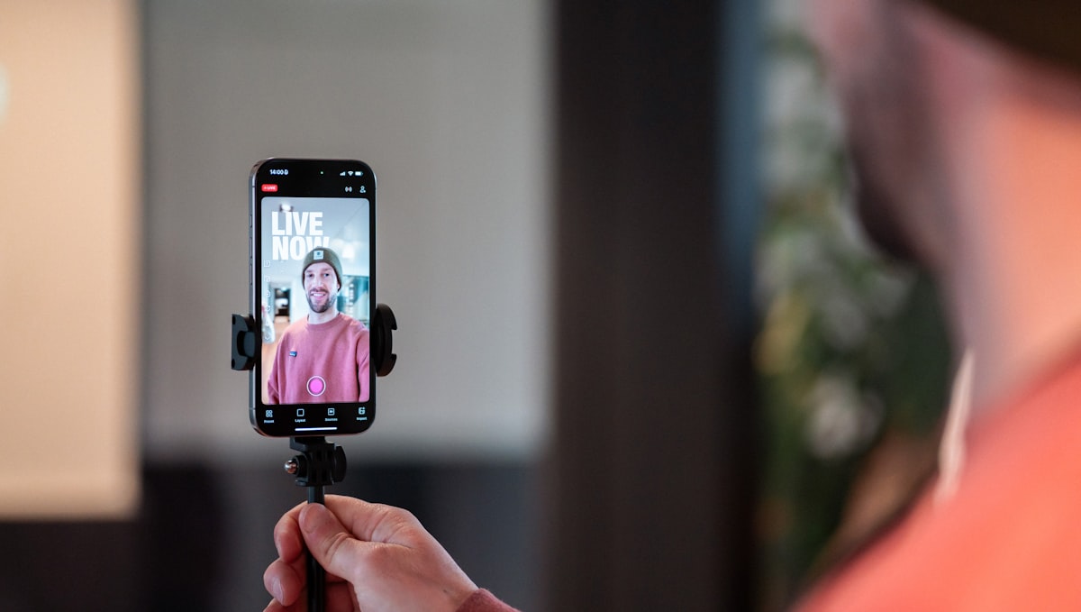 Ersteller nutzt Smartphone auf Stativ für Live-Videostreaming mit LIVE NOW auf dem Bildschirm